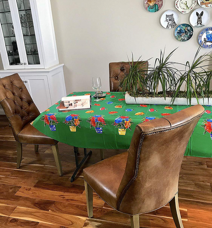 Angle view: Multi-colored flower print on green background tablecloth, open book displayed with potted plant centerpiece.