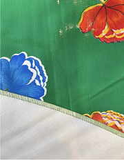 Close up: Multi-colored flower print on green background tablecloth with white underside folded up to show contrast.