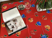 Above view: Multi-colored flower print on red background tablecloth, opened book displayed and potted plant centerpiece.