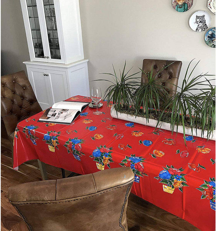 Angle view: Multi-colored flower print on red background tablecloth, opened book displayed and potted plant centerpiece.