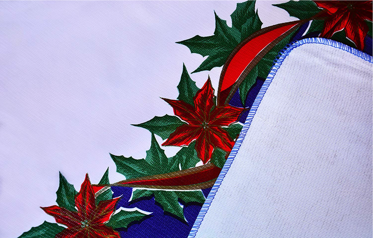 Close up: Red ribbons with poinsettia edging on white and blue striped background tablecloth with white underside folded up to show contrast.