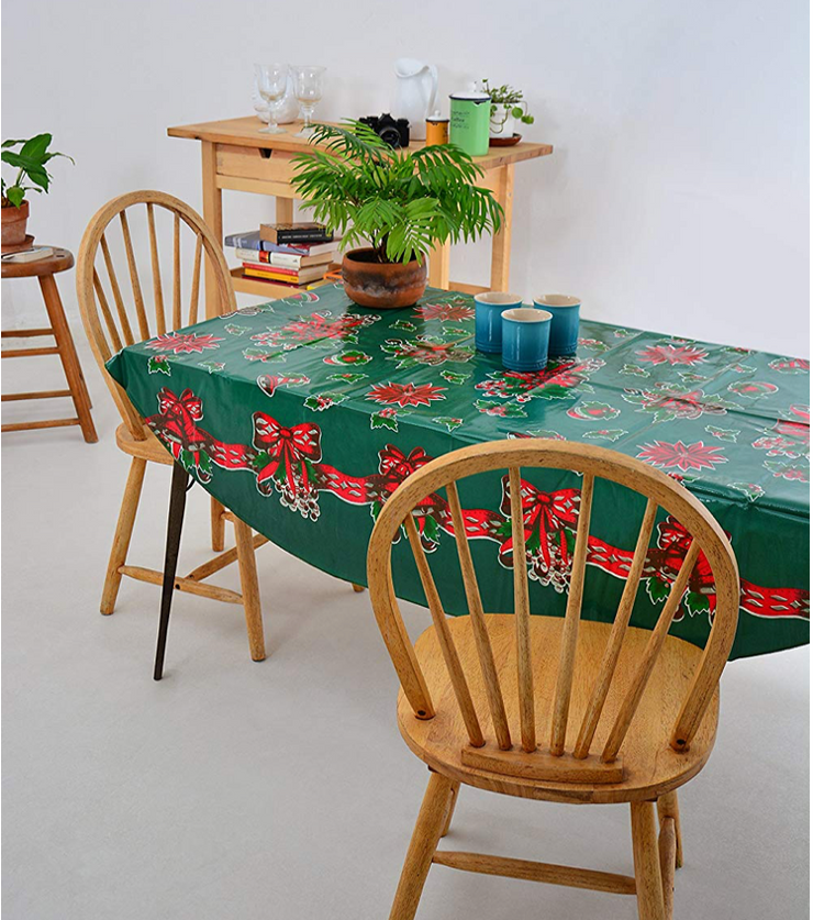 Angle view: Multi-colored Christmas holiday print on green background tablecloth, with potted plant centerpiece.