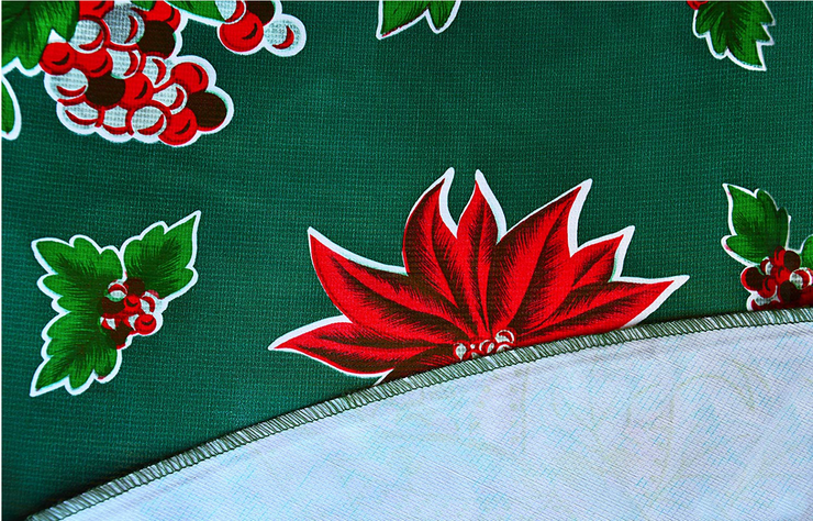 Close up: Multi-colored Christmas holiday print on green background tablecloth with white underside folded up to show contrast. 