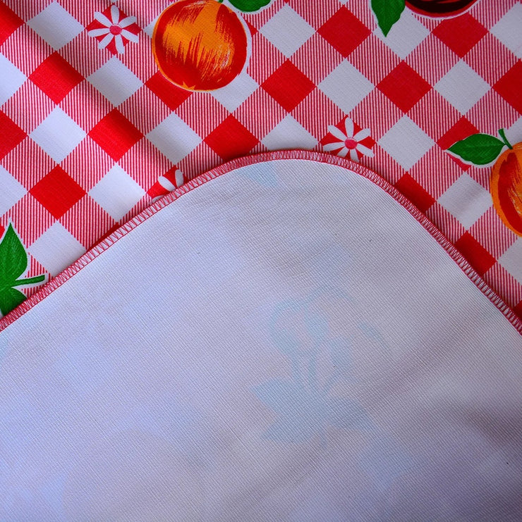 Close up:  Multi-colored fruit print on red and white checkered pattern background tablecloth with white underside folded up to show contrast.