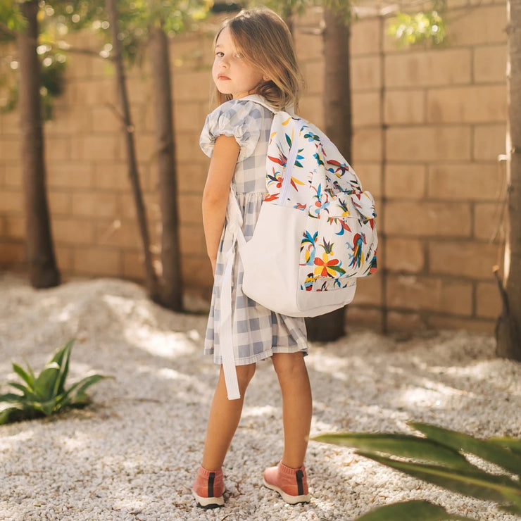 A young girl wears Otomi backpack with multi-colored flower/animal print on white background.