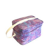 Angle view: Pink, blue and purple splatter print lunchbox with white strap handle. 