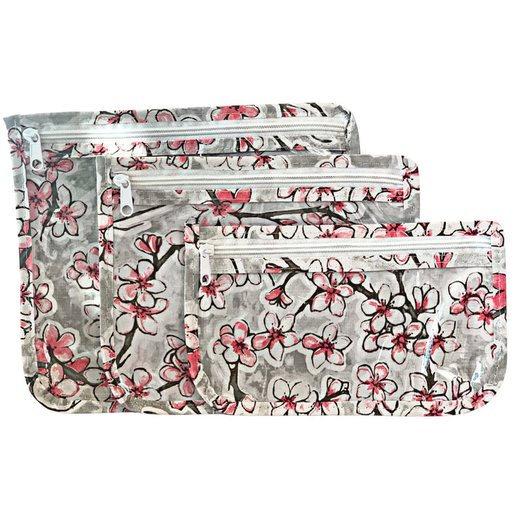 Front view: Small, medium and large slim travel bags, white zippers and cherry blossom print on a gray background.